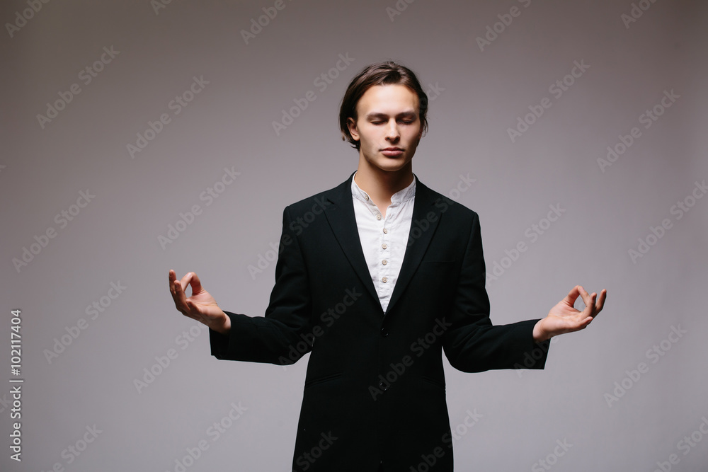 Meditative young businessman on a gray background Meditative young businessman on a gray background