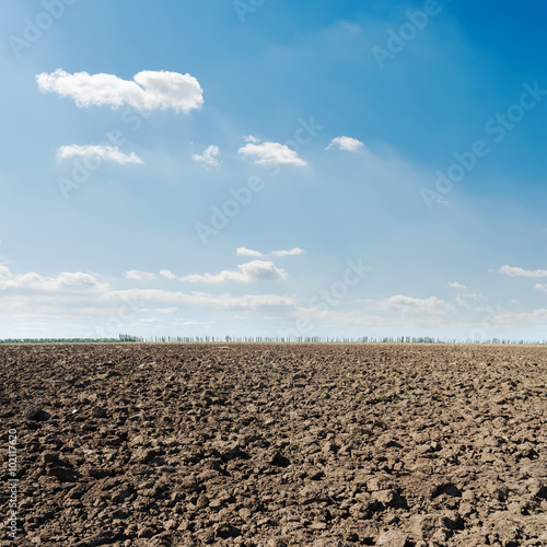 black plowed field and blue sky with clouds