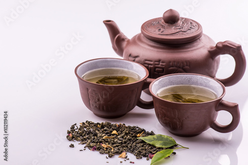 Green tea in a cup and teapot, petals of green tea on a bamboo mat on a white background