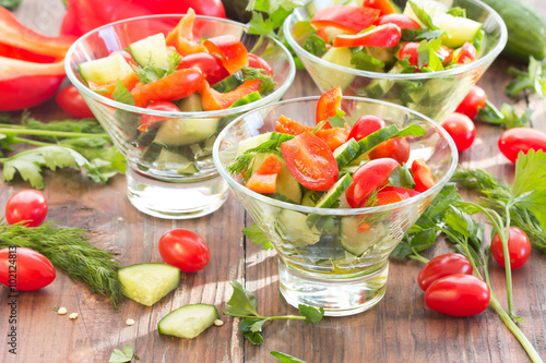 Three glass bowls with a salad of fresh vegetables and ingredients - tomato, cucumber, bell pepper on a dark wooden background 