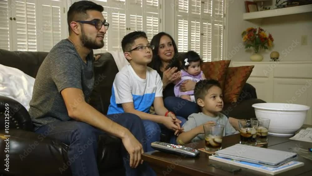 An attractive Hispanic family with two cute boys enjoying popcorn as they all watch TV together. An attractive Hispanic family with two cute boys enjoying popcorn as they all watch TV together.