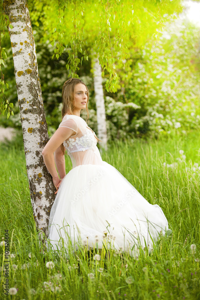 Junge romantische Frau lehnt in Hochzeitskleid an Baum Junge romantische Frau lehnt in Hochzeitskleid an Baum