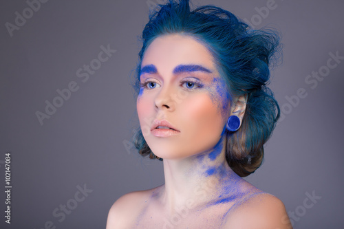 Gorgeous young woman with blue hair, earrings, makeup on a gray background in the studio