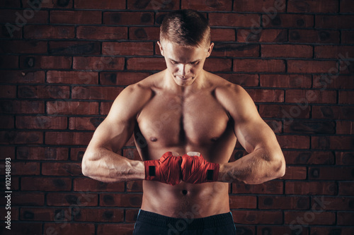 Muscular Fighter With Red Bandages against the background of a brick wall