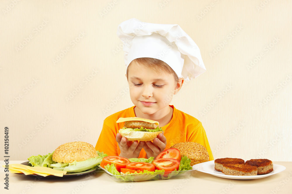 Little smiling boy in chefs hat preparing a hamburger Little smiling boy in chefs hat preparing a hamburger