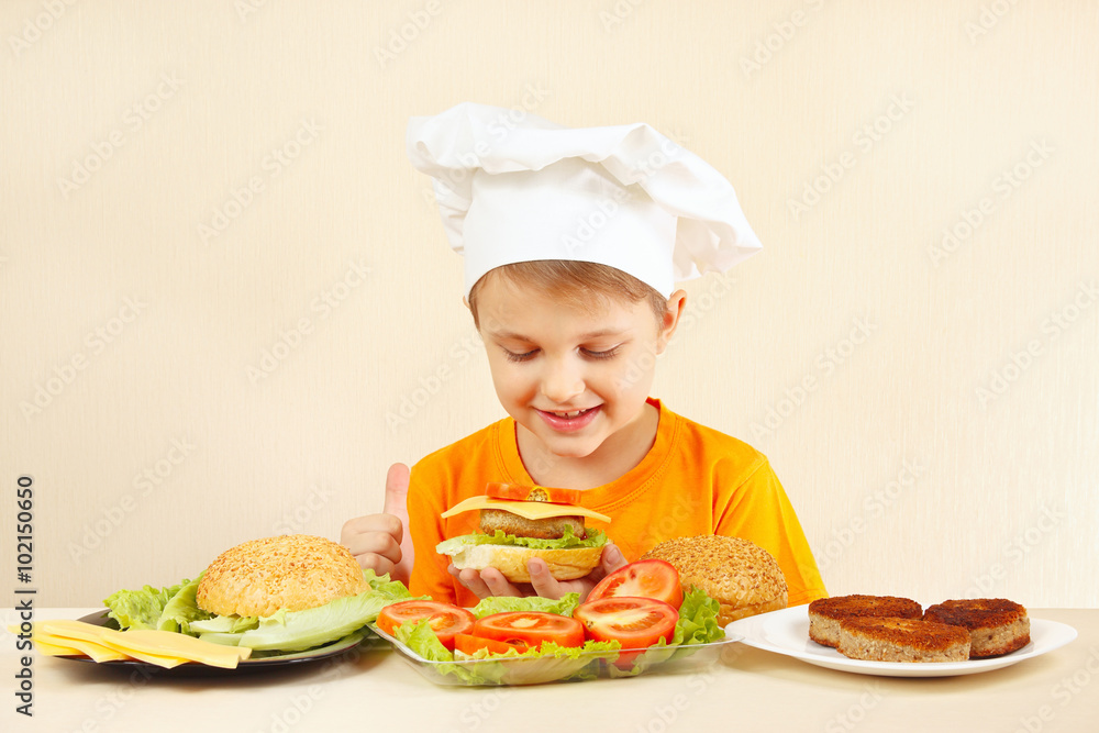 Little funny chef in chefs hat preparing a hamburger Little funny chef in chefs hat preparing a hamburger