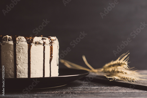 Creamy cake with chocolate glaze on the rustic background. Toned image.