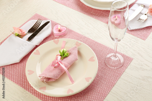 Table setting with dishes, cutlery, napkin and candles on pink background