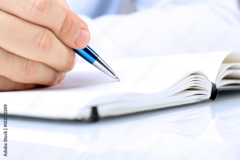 businessman writing in a notebook while sitting at a his desk businessman writing in a notebook while sitting at a his desk