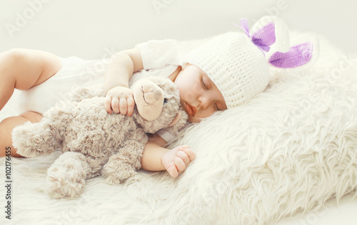 Cute baby sleeping with teddy bear toy on white soft bed at home