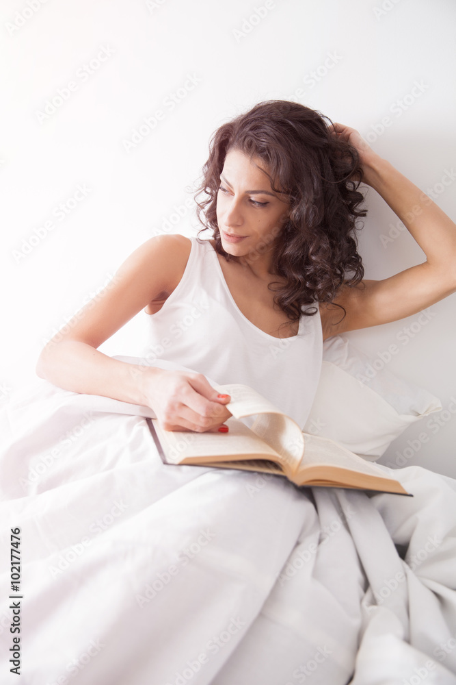 Brunette long hair woman under the duvet reading a book Brunette long hair woman under the duvet reading a book