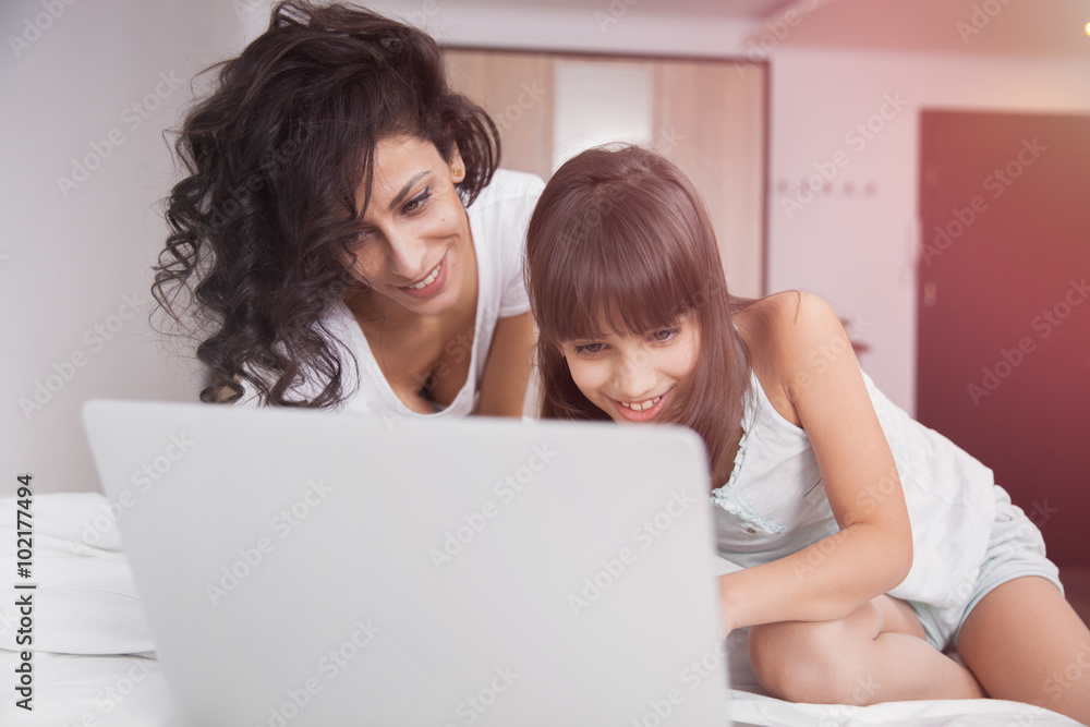 Brunette long hair mother and daugther on the bed with a laptop computer Brunette long hair mother and daugther on the bed with a laptop computer