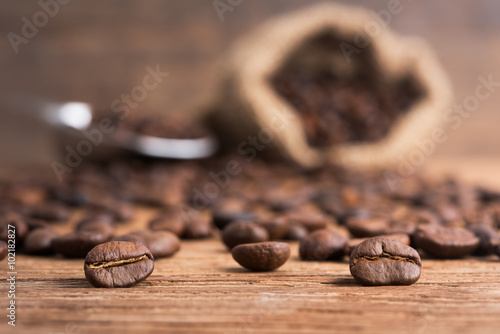 A coffee beans on the stainless scoop and coffee bag on the wooden table