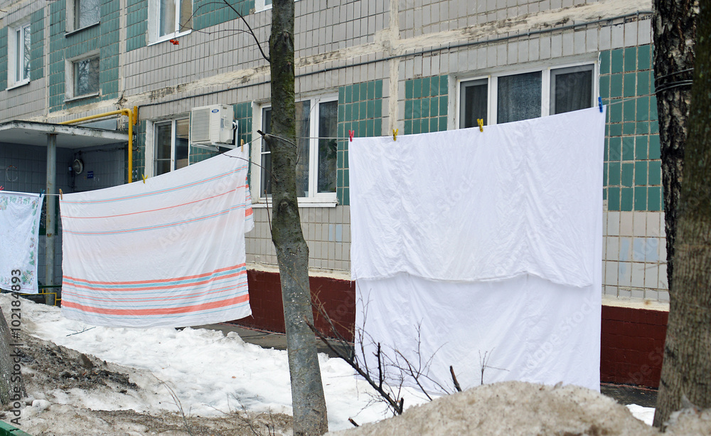 Чистое постиранное бельё сушится на веревке на улице под окнами жилого домазимой фотография Stock