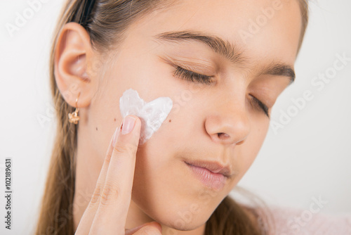 Portrait of young girl applying cream on her pretty face. girl with cream on her cheek. heart on the cheek 