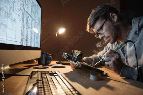 Focused man repairing motheboard with soldering iron photo