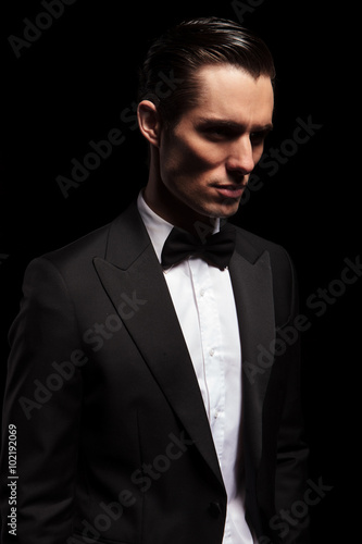 classy man in tuxedo looking away in dark studio