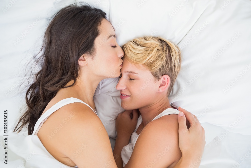 Woman lying and kissing her girlfriend on forehead Woman lying and kissing her girlfriend on forehead