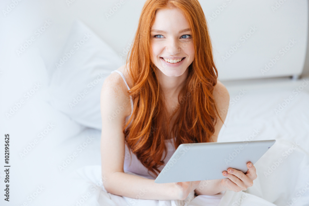 Cheerful woman sitting on bed and using laptop Cheerful woman sitting on bed and using laptop