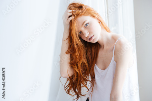 Fotografie, Obraz Sensual woman with beautiful red hair standing near window