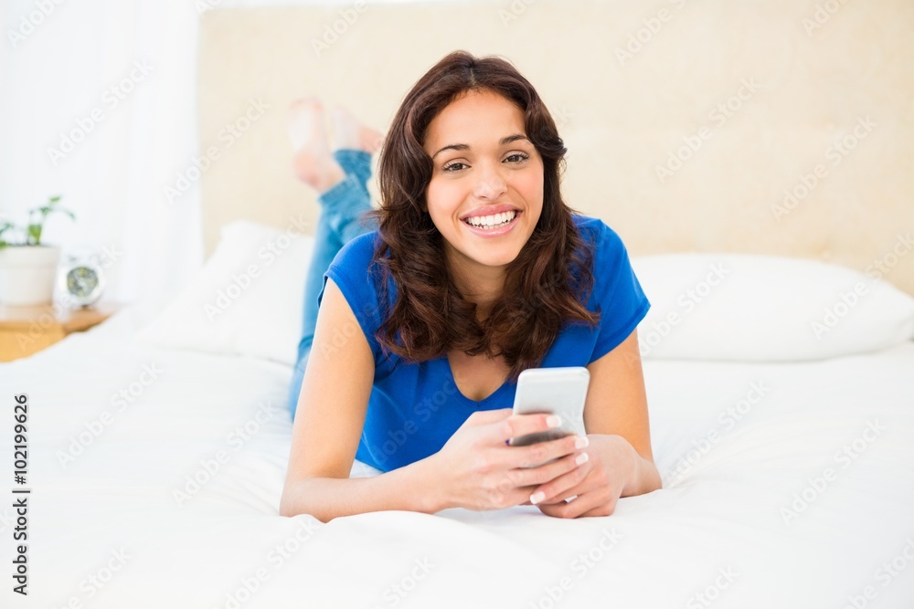 Smiling woman using smartphone while lying on bed Smiling woman using smartphone while lying on bed