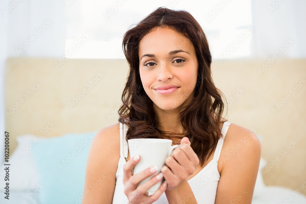 Happy woman holding cup of coffee while sitting on bed Happy woman holding cup of coffee while sitting on bed