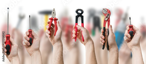 Many hands holds up instruments and tools on blurry background.
