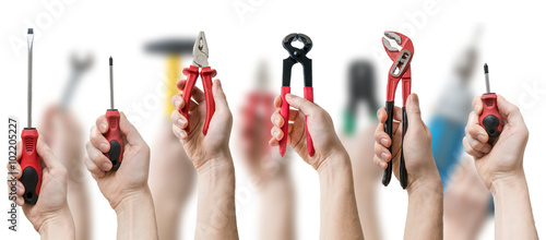 Many hands holds up instruments and tools on blurry background.