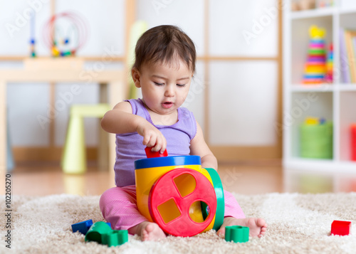 toddler girl playing indoors with sorter toy sitting on soft carpet