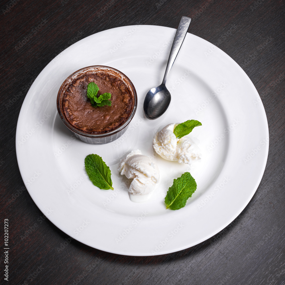 Warm dessert chocolate fondant lava cake served with vanilla ice cream balls and mint on white plate. Famous French dessert on dark wooden table top view