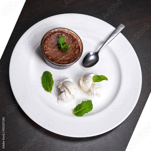 Warm dessert chocolate fondant lava cake served with vanilla ice cream balls and mint on white plate. Famous French dessert on dark wooden table top view.