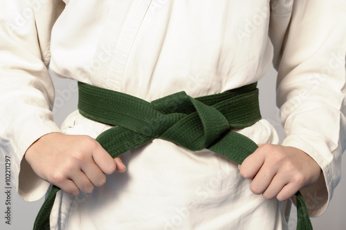 Hands tightening green belt on a teenage dressed in kimono for martial arts. Sepia toning