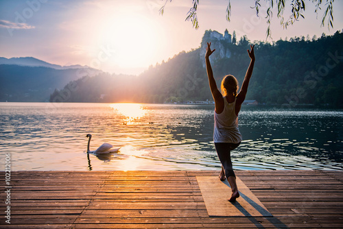 Sun Salute Yoga. Young woman doing yoga by the lake at sunset, swan passing by