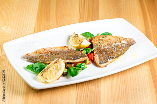 Tasty baked fish with grilled vegetables on  plate on wooden table close-up