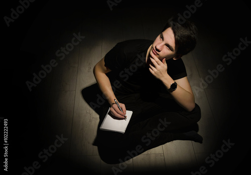 Teenager young man thinking and writing on notebook on black bac