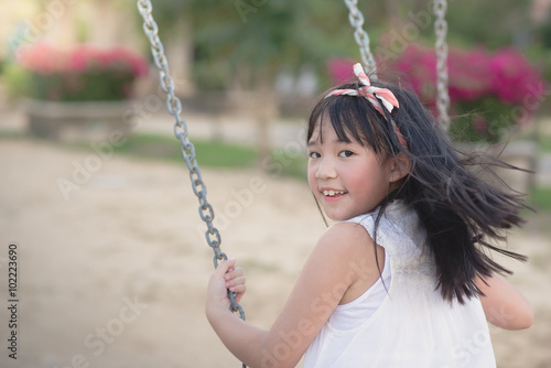 Beautiful asian girl swinging on the playground