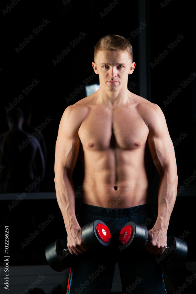 Handsome power athletic man with dumbbell confidently looking forward. Strong bodybuilder six pack, perfect abs, shoulders, biceps, triceps and chest Handsome power athletic man with dumbbell confidently looking forward. Strong bodybuilder six pack, perfect abs, shoulders, biceps, triceps and chest