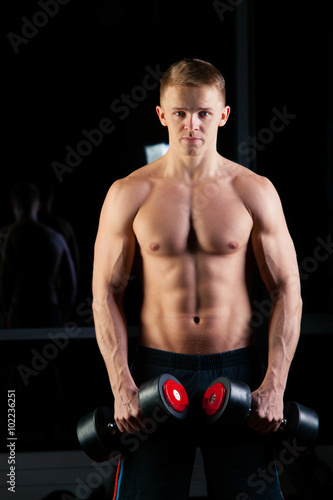 Handsome power athletic man with dumbbell confidently looking forward. Strong bodybuilder six pack  perfect abs  shoulders  biceps  triceps and chest