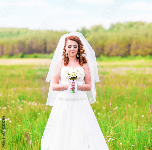 Beautiful bride with wedding bouquet of flowers outdoors in field