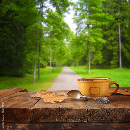 front image of coffee cup over wooden table in front of forest background 
