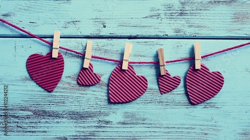 cinemagraph of some hearts, made with red corrugated paperboard, swaying in a clothes line, against a blue background