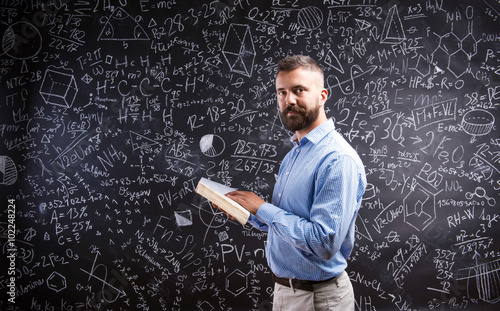 Teacher with book against big blackboard with symbols and formul photo