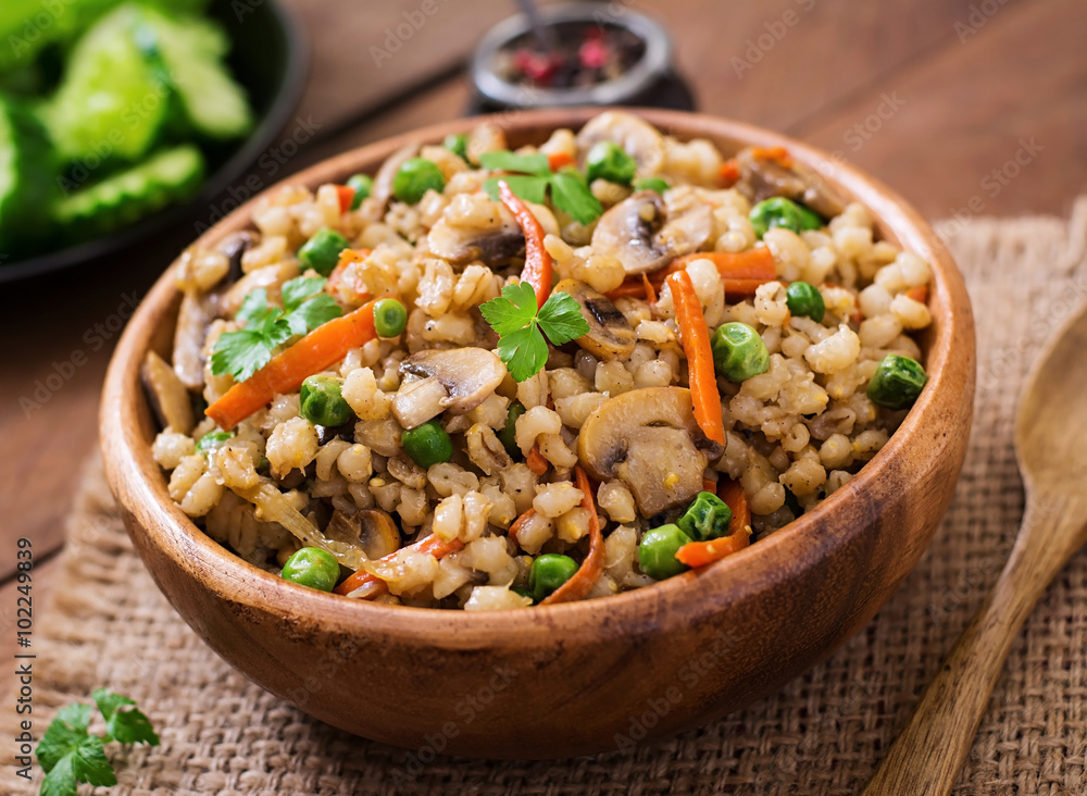 Vegetarian crumbly pearl barley porridge with mushrooms and green peas in a wooden bowl Vegetarian crumbly pearl barley porridge with mushrooms and green peas in a wooden bowl