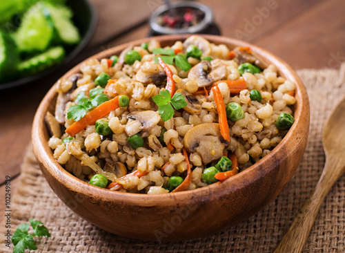 Vegetarian crumbly pearl barley porridge with mushrooms and green peas in a wooden bowl