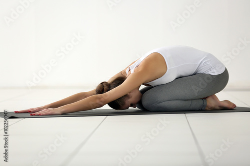Health concept. Young attractive woman does yoga exercise in the gym against white wall