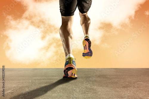strong athletic legs with ripped calf muscle of young sport man running on grunge asphalt road at orange sunset sky