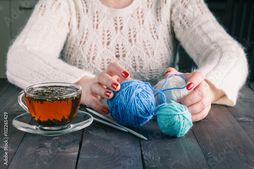 Woman hands with cup of tea and wool yarn balls on a wooden tabl