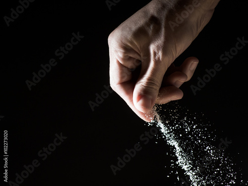 Hand spilling a pinch of salt against black background