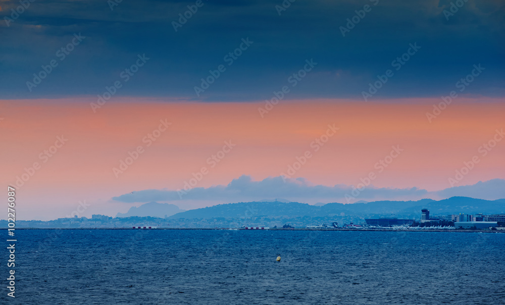 France, Nice, 2015.09.12: International airport at the sunset, mediterranean sea, lights arriving and departing aircraft, pink sky