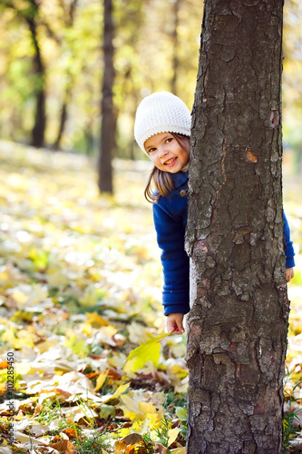 Cute little girl peeking from behind a tree.